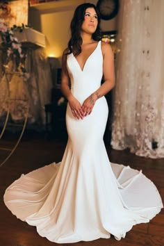 a woman in a white wedding dress standing on a wooden floor with her hands behind her back