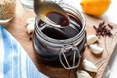 a wooden cutting board topped with lots of food and a jar filled with liquid next to garlic