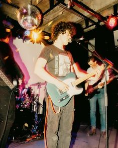 a young man playing guitar while standing in front of a microphone and singing into a mic