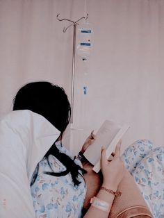 a woman laying in bed reading a book with an iv drip attached to the wall behind her