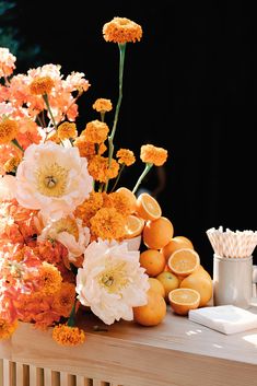 an arrangement of flowers, oranges and strawberries are sitting on a wooden table