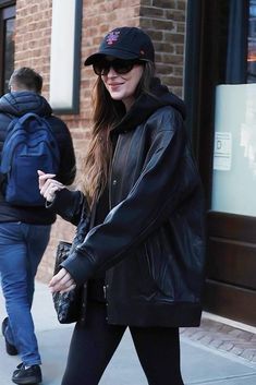 a woman in black jacket and leggings walking on sidewalk next to brick building