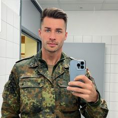 a man in uniform taking a selfie with his cell phone while standing in front of a mirror