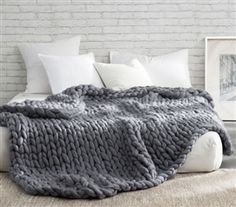 a large gray blanket sitting on top of a white bed next to pillows and blankets