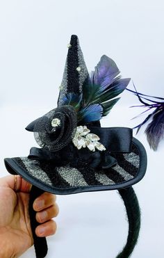 This Witch Hat Fascinator is an easy and classy way to dress up this year! This is a black and silver witch hat that is attached to a black yarn wrapped headband. The hat is adorned with ruffled lace, a netted flower, rhinestones and iridescent feathers. Will Fit a 4 year old and up! Like our Facebook Page and get 10% off when you message me before checkout! Everything made by handmade MKE is one of a kind and unique, however, if you would like a different size or see a piece that you would like Tiny Witch Hat, Bad Witch Costume, Witch Hat Headband, Iridescent Feathers, Witch Hats Costume, Modern Day Witch, Witch Hair, Easy Halloween Costume, Fancy Dress Halloween Costumes