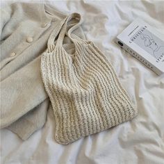 a knitted bag sitting on top of a bed next to a book and sweater