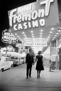 a man and woman walking down the sidewalk in front of a casino