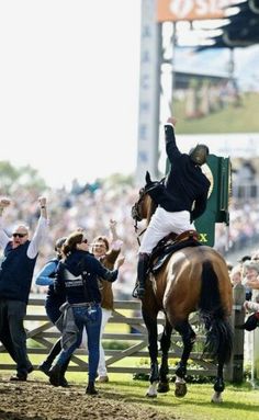 a man riding on the back of a brown horse in front of a group of people