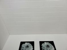 two black and white pictures with flowers on them in a room that is painted white