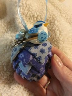 a hand holding a blue and white bird ornament on top of a blanket