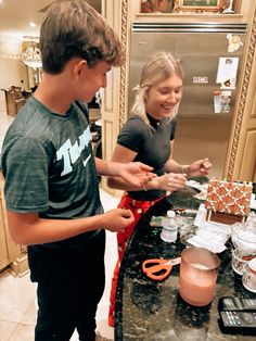 a man and woman standing in front of a kitchen counter making gingerbread house decorations