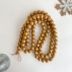 a wooden bead necklace next to a metal can and snowflake on a white surface