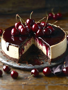 a cheesecake topped with cherries on top of a wooden table