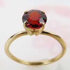 "A deep red-orange Almandine garnet tops this vintage 14k yellow gold solitaire ring. Four sturdy prongs hold the 6.6mm x 4.9mm garnet in a raised crown setting. The 1.64 carat garnet is a lovely deep orangeish-red color with nice sparkle and clean facets. The ring was finished with a sturdy classic band. The inside is signed with a connected double \"S\" and \"14k\" (gold) in the center. This piece would make a lovely birthstone gift for the person with a January birthday or a unique engagement Classic Garnet Rings With Prong Setting, Classic Rings With Garnet And Prong Setting, Classic Garnet Solitaire Rings, Classic Solitaire Garnet Ring, Formal Solitaire Ruby Ring With Round Stone, Formal Solitaire Ruby Ring With Round Cut, Classic Ruby Ring With Tension Setting, Classic Round Ruby Ring With Tension Setting, Classic Garnet Round Cut Ring