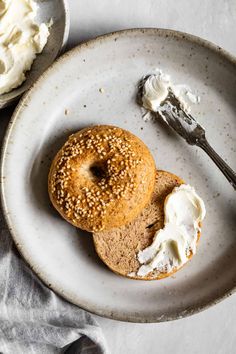 two bagels on a plate with cream cheese and a fork next to them,