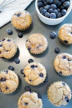 blueberry muffins are sitting on a baking sheet next to a bowl of blueberries