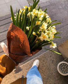 a bouquet of daffodils in someone's feet on the ground next to a sidewalk