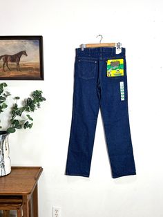 "Deadstock jeans by Wrangler, circa early-mid 2000s. Slim fit, especially through the hips. Slight boot cut. Never washed or worn. Tags still attached.  Label: Wrangler  Fabric: 100% cotton  Marked size: 31x32  Fits: up to 31-32\" waist max -- see measurements below for most accurate fit -- jeans have never been worn/washed and may shrink slightly upon first laundering  Condition: excellent | old stock | never worn  Waist 32 inches  Rise 11.5 inches  Inseam 32.25 inches  Hips 37 inches  Thigh 22 inches  Ankle 16 inches" Straight Leg Denim Blue Jeans For Rodeo, Cotton Straight Leg Jeans For Rodeo, Denim Blue Straight Leg Bottoms For Rodeo, Dark Wash High Rise Jeans For Rodeo, High Rise Dark Wash Jeans For Rodeo, High Rise Cotton Jeans For Rodeo, Vintage Dark Wash Jeans For Rodeo, Vintage Straight Leg Rodeo Bottoms, Vintage Straight Leg Bottoms For Rodeo