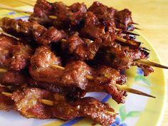 several skewers of meat sitting on top of a yellow and blue plate with chopsticks