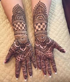 two hands with henna tattoos on them sitting on top of a white bed next to each other