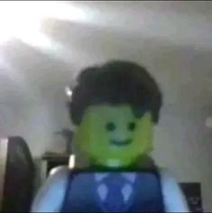 a man in a suit and tie standing next to a giant green lego figure with a smile on his face