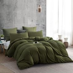 a bed with green comforters and pillows in a room next to a white table