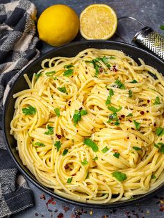 a bowl filled with pasta and topped with parsley next to lemons, pepper flakes and seasoning