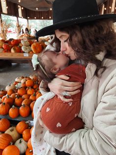 a woman holding a baby in her arms while surrounded by lots of pumpkins and squash