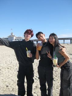 three people standing on the beach with drinks in their hands and one person pointing at something