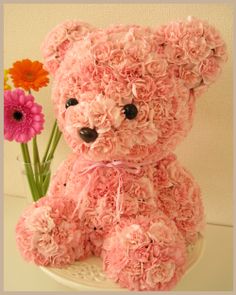 a pink teddy bear sitting next to some flowers