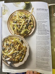 an open magazine with two plates of food on it and a hand holding a fork