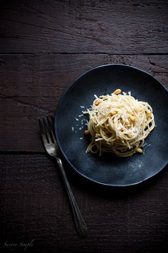 a black plate topped with pasta and parmesan cheese on top of a wooden table