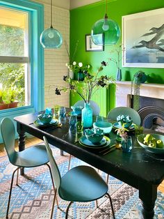 a dining room with green walls and blue chairs around the table in front of a fireplace