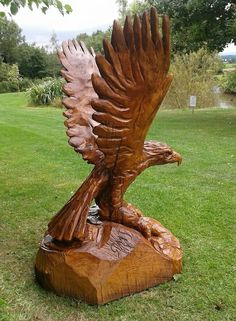 a wooden sculpture of an eagle on a rock in the middle of a grassy field