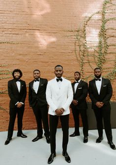 a group of men in tuxedos standing next to each other near a brick wall