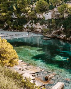 people are swimming in the clear blue water near some cliffs and trees on either side