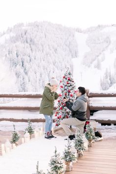 two people are decorating a christmas tree in the snow while another person takes pictures