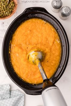 an overhead view of a bowl of carrot soup with a spoon in it and other ingredients around the bowl