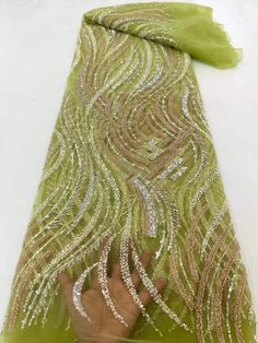 a hand is reaching up to the side of a piece of green fabric with gold and silver sequins on it