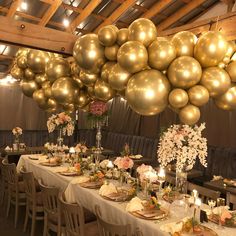 a long table with gold balloons hanging from it's ceiling and flowers on the tables