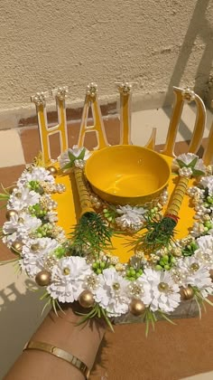 a yellow bowl sitting on top of a table surrounded by white flowers and gold letters