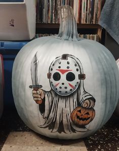 a painted pumpkin with a hockey mask on it and a person holding a knife in one hand