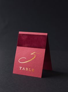 a red table card with a gold arrow on the front and an embossed logo on the back