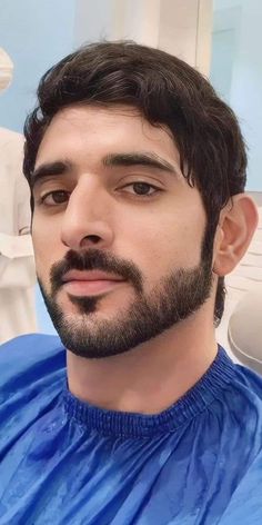 a close up of a man with a beard in a blue shirt looking at the camera