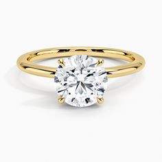 a yellow gold engagement ring with a round cut diamond in the center, on a white background