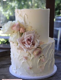 a wedding cake with white frosting and pink flowers on top is sitting on a wooden table