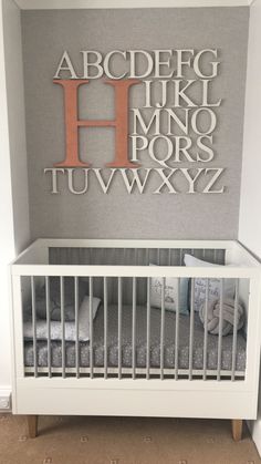 a white crib in front of a gray wall with the letter h on it