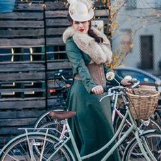 a woman is standing next to her bike wearing a hat and coat with feathers on it