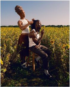 two people sitting in a field of sunflowers one is cutting the other's hair