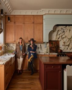 two women standing in a kitchen with wooden cabinets and marble counter tops on the island